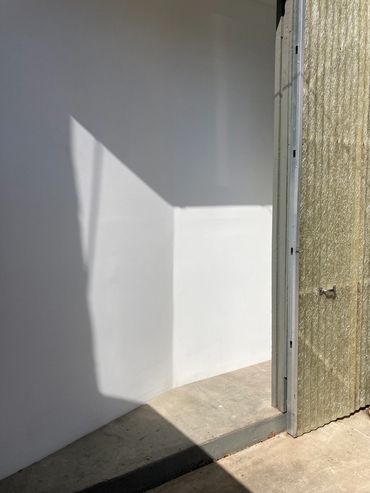 Sunlight casting geometric shadows on a white wall and concrete floor.