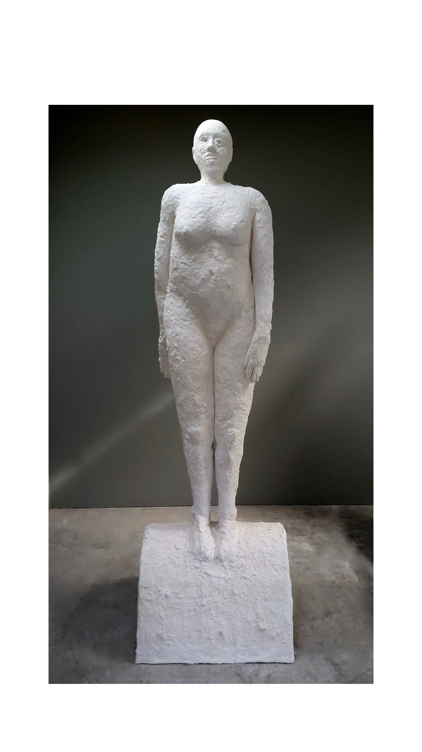 White textured sculpture of a standing nude human figure on a pedestal.