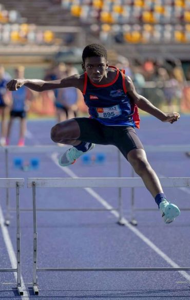Young athlete clearing a hurdle on a track.