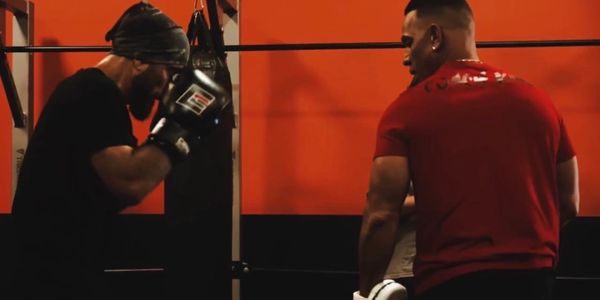 Two men training in a boxing gym with gloves and focused stances.