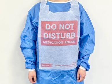 Person wearing a protective gown with a 'Do Not Disturb' apron.