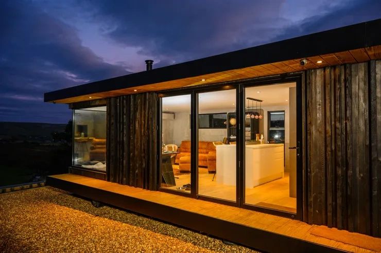 Modern cabin with warm interior lighting at dusk.