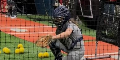 A young baseball catcher in gear prepares to catch balls indoors.