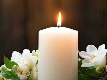 A lit white candle surrounded by white flowers.
