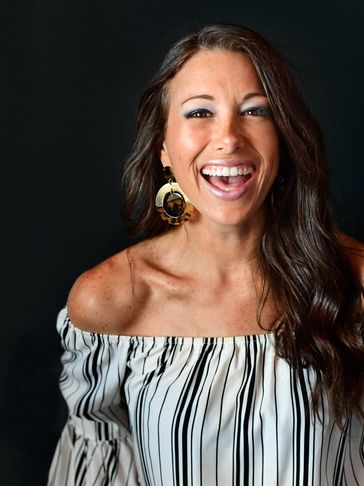 Smiling woman with long hair wearing striped off-shoulder top and large earrings.