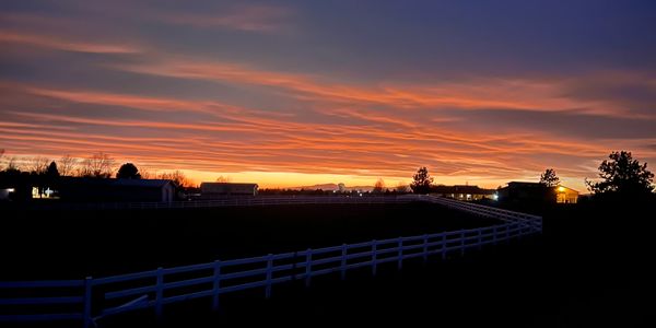 Sunset over a rural landscape with silhouetted trees and fences.