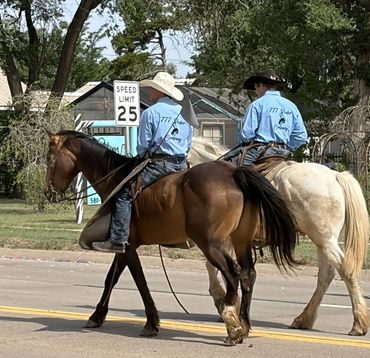 Two riders on horses crossing a street with a speed limit sign.