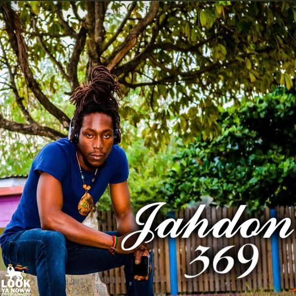 A man with dreadlocks and headphones sitting outdoors under a tree.