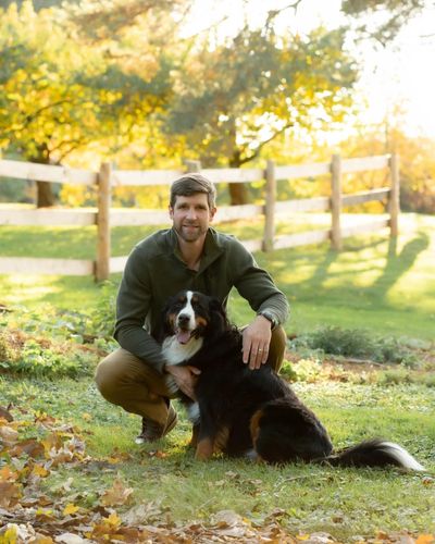 Man squatting outdoors hugging a large dog.