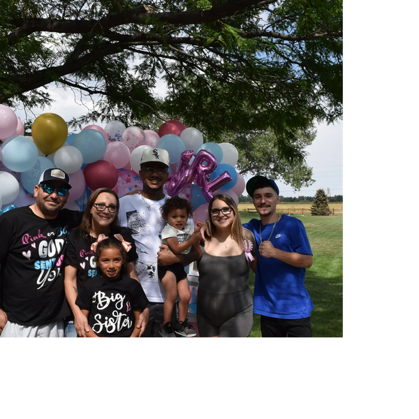 Family gathered outdoors with balloons for a gender reveal party.