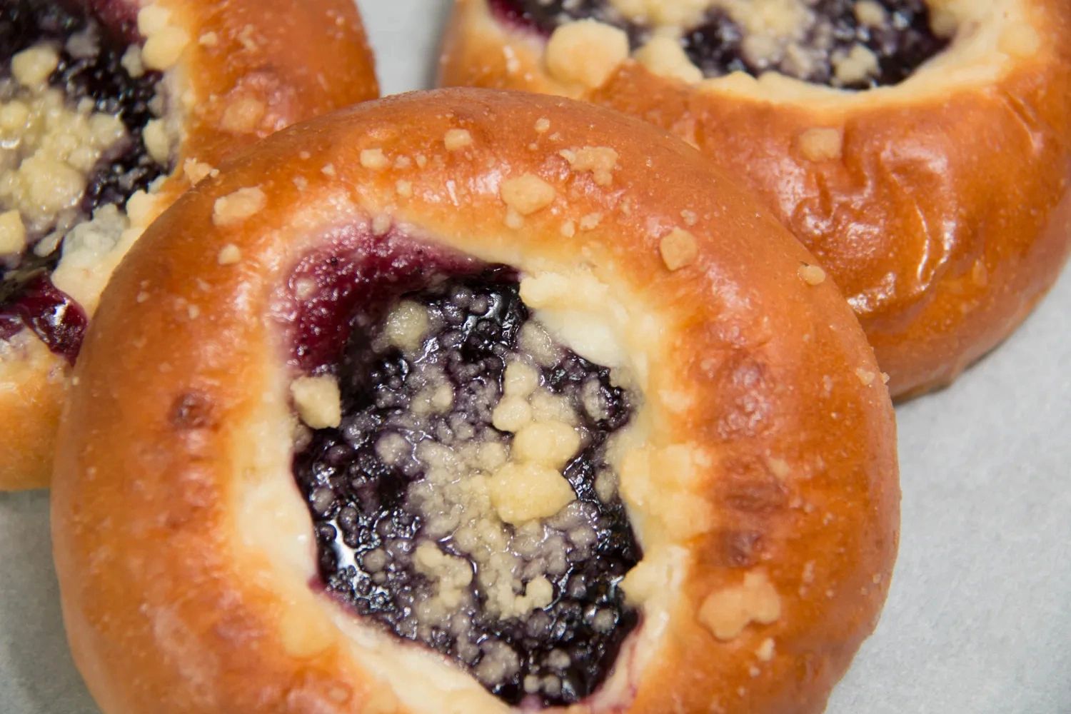 Close-up of three round pastries with blueberry filling and crumb topping.