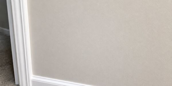 Close-up of a beige wall with white baseboard and carpeted floor.