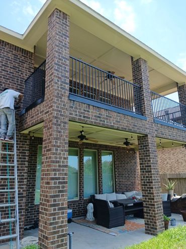 A man on a ladder working on the balcony of a brick house.
