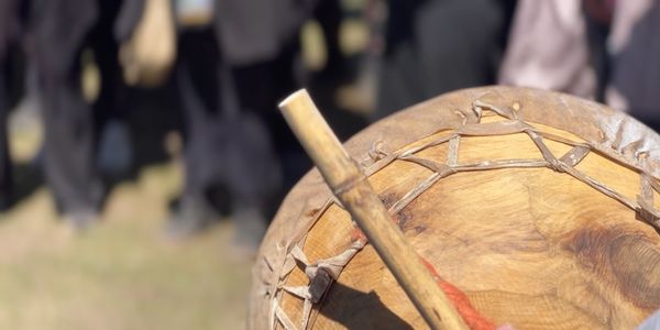 Close-up of a wooden drum with a drumstick outdoors.
