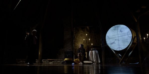 A dimly lit room with two figures and a large illuminated circular screen.