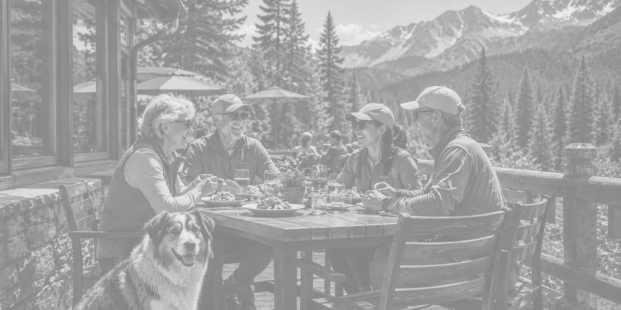 Four people and a dog enjoying a meal outdoors in the mountains.