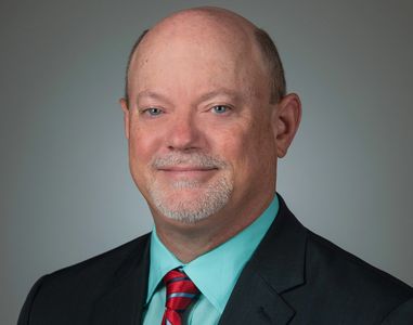 Professional portrait of a bald man in a suit with a red striped tie.