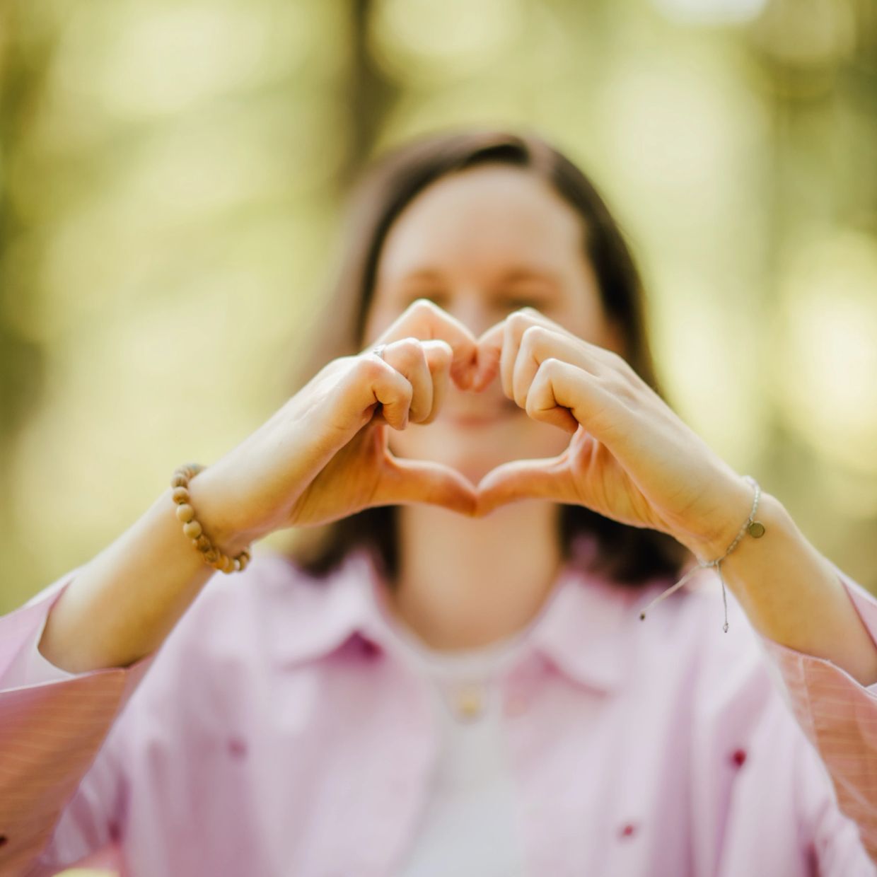 Woman forming a heart shape with her hands in soft focus.