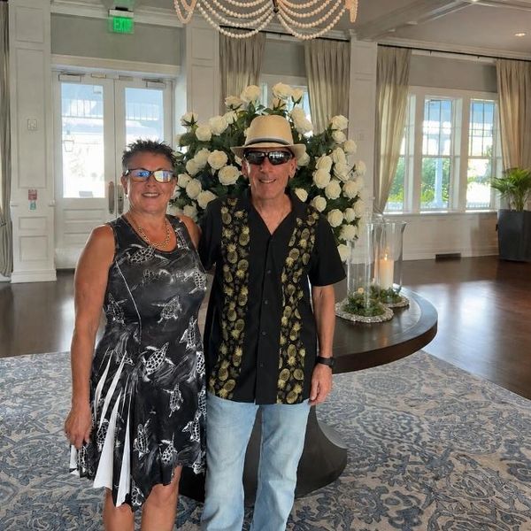 A smiling couple posing indoors with white flowers and chandelier.