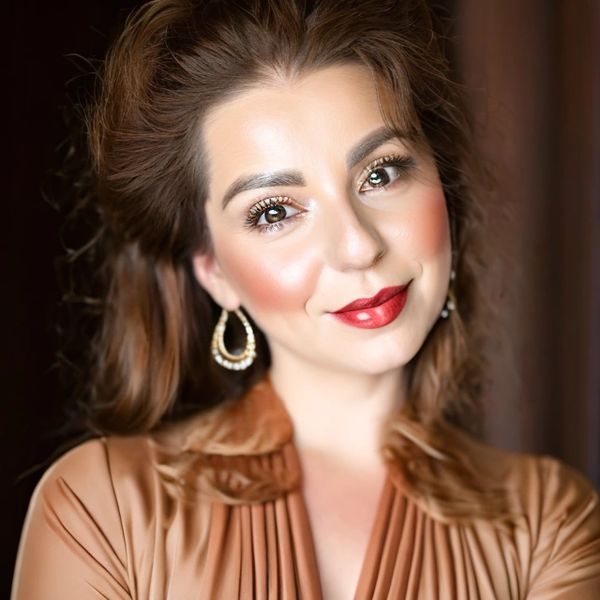 Elegant woman with flawless makeup and red lipstick smiles warmly.