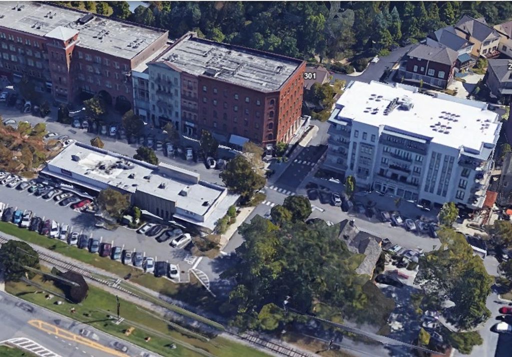 Aerial view of urban buildings, parking lots, and greenery with a railway track in the foreground.