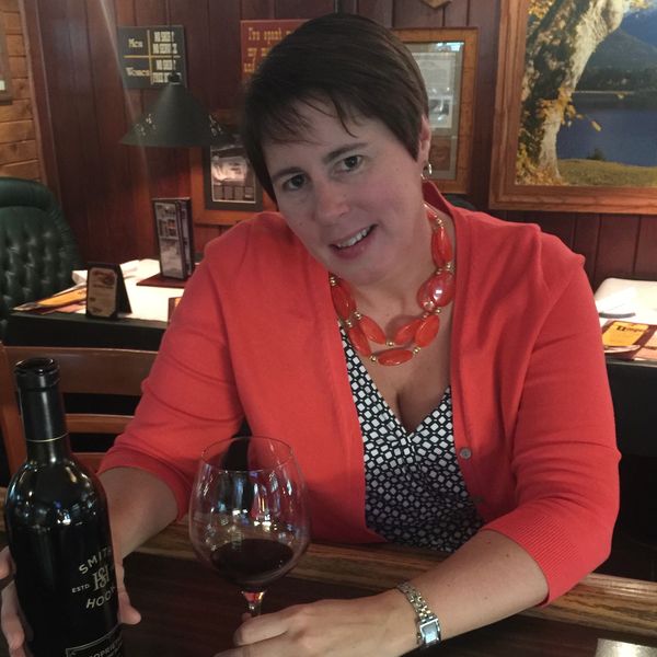 Woman in orange cardigan holding wine glass at a bar.