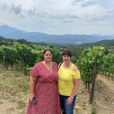 Two women posing in a vineyard with mountains in the background.