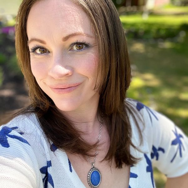 Smiling woman outdoors wearing a blue and white top with a pendant necklace.