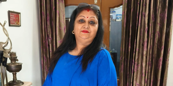 Woman with long black hair in a blue top indoors.
