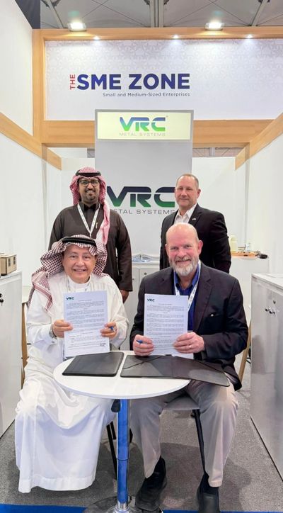 Four men at SME Zone booth holding signed documents for VRC Metal Systems.