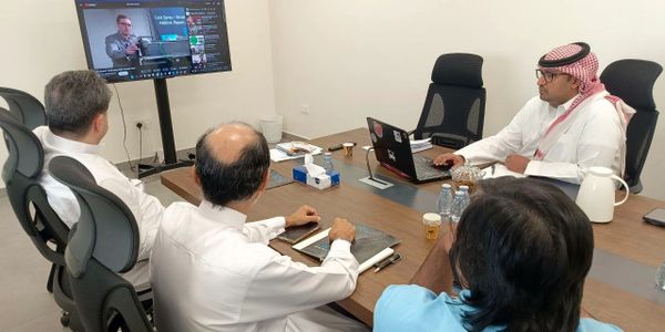 Four men in a meeting watching a presentation on a screen.