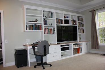 Modern home office with built-in shelves, desk, and TV.