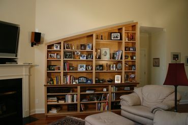 Cozy living room with a slanted wooden bookshelf filled with books and photos.