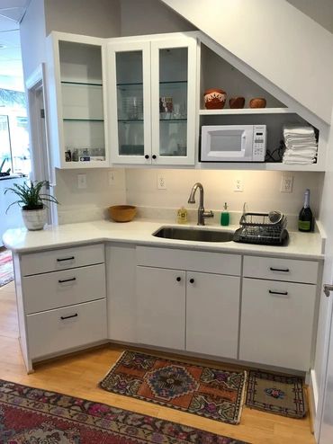 Compact kitchenette with white cabinets, a microwave, and decorative rugs.