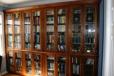 Wooden bookshelf with glass doors filled with books and trophies.