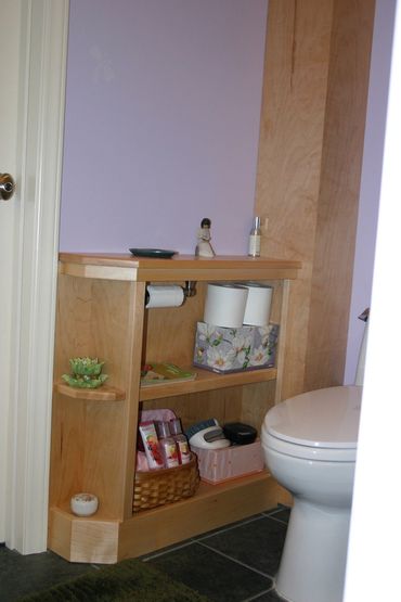 Maple bathroom shelf with toiletries and toilet paper beside a toilet.