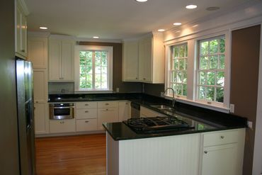 Modern kitchen with black countertops and white cabinets under large windows.