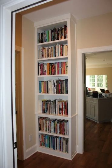 Built-in tall bookshelf filled with books in a narrow corner.