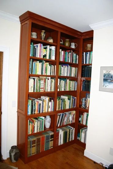 Wooden corner bookshelf filled with books and pottery.