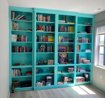Turquoise bookshelf filled with books and decorative items in a sunlit room.
