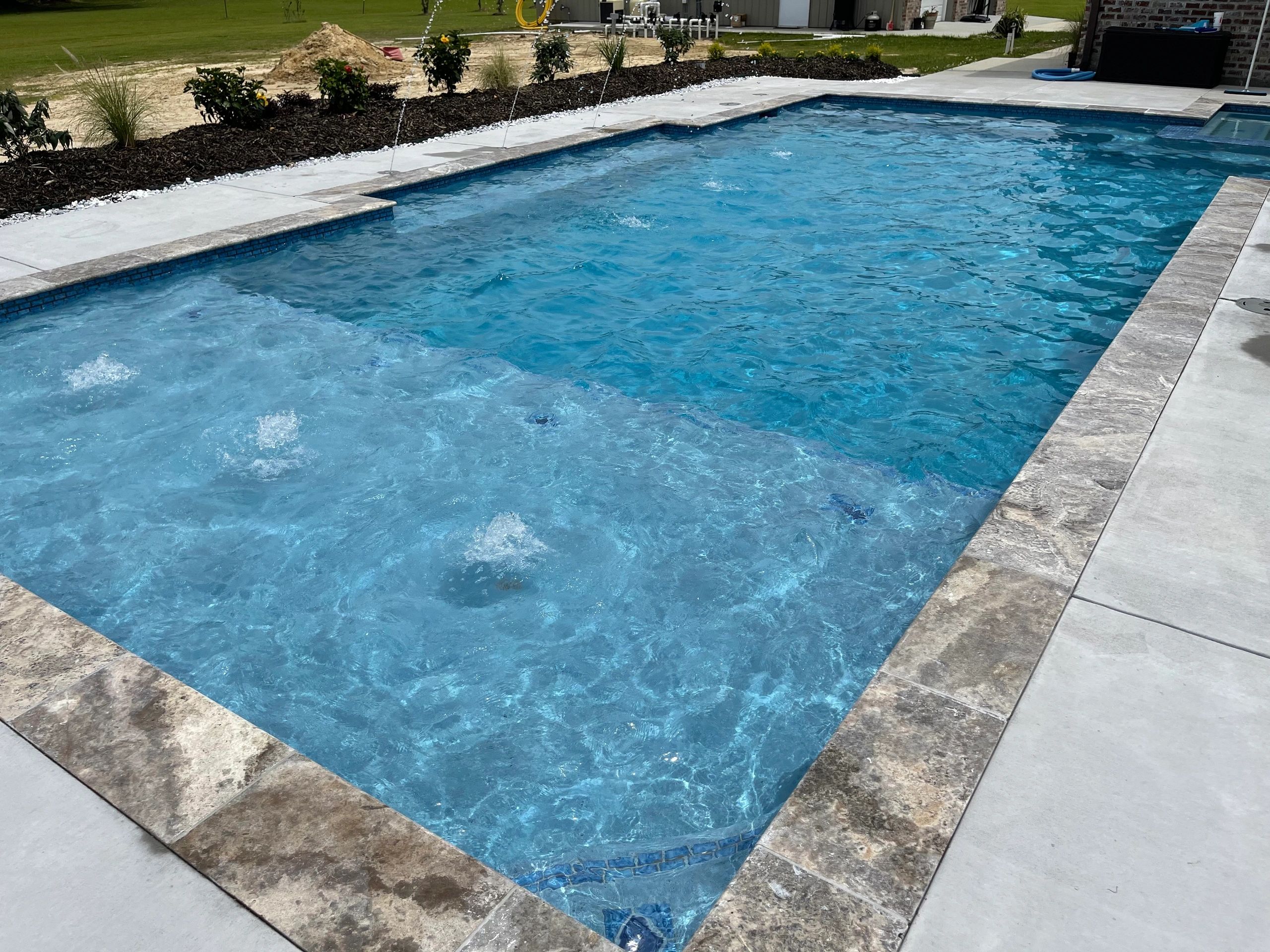A clear, blue swimming pool with water jets and a surrounding stone deck.
