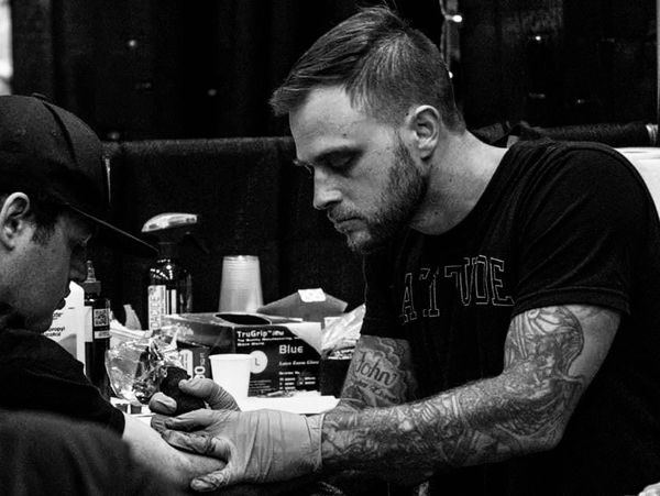 Tattoo artist focused on tattooing a client's hand in a black and white photo.