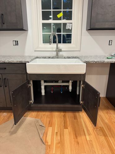 Modern kitchen sink with open cabinet doors showing plumbing.