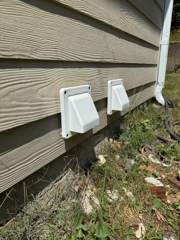 Two white vent covers on a beige wooden house exterior.
