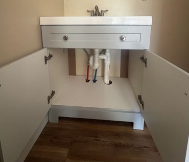 Open bathroom cabinet showing plumbing and pipes under the sink.