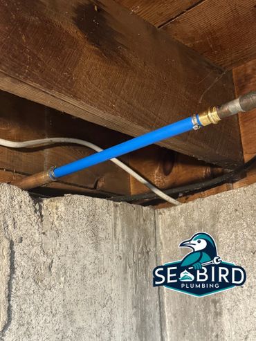 Blue plumbing pipe installation in a wooden basement ceiling.