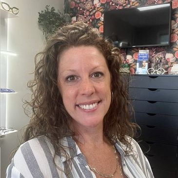 A smiling woman with curly hair in a floral-themed room.