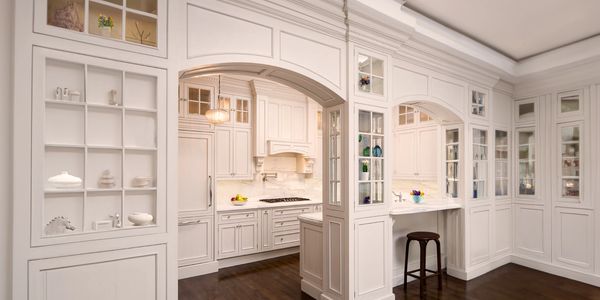 Kitchen with extensive white cabinetry, leading into dining room with built-in glass fronted cabinet