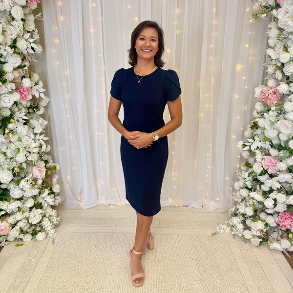 Woman in a black dress smiling between floral decorations.