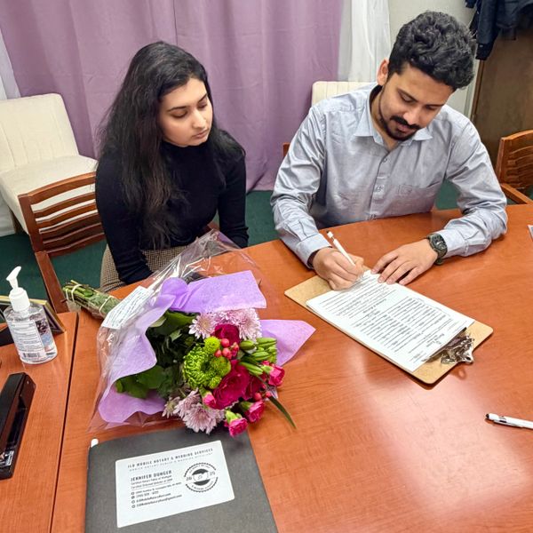 A couple signing documents at a table with flowers and sanitizer.